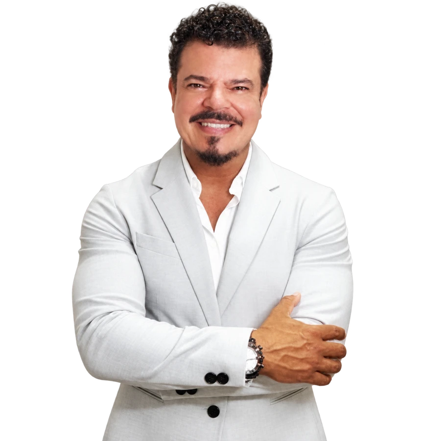 Adriano Menezes, sonriendo, con chaqueta clara y los brazos cruzados.
